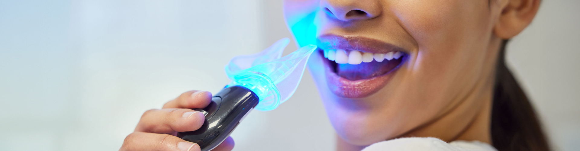 Woman using blue LED light for professional teeth whitening treatment at a dental office.